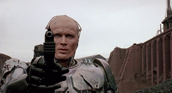 RoboCop (Peter Weller) unmasked, aims his Auto-9  
at Boddicker.